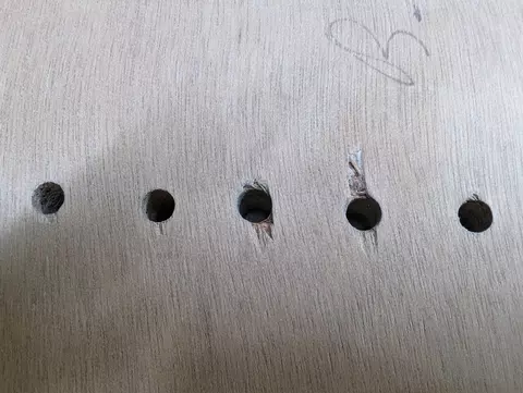 Row of six holes in wood, one with a screw and another with splintered edge