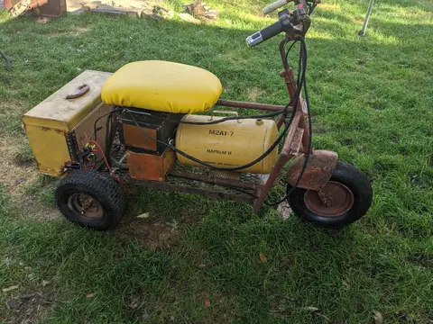 Vintage yellow Cushman scooter with seat parked on grass outdoors